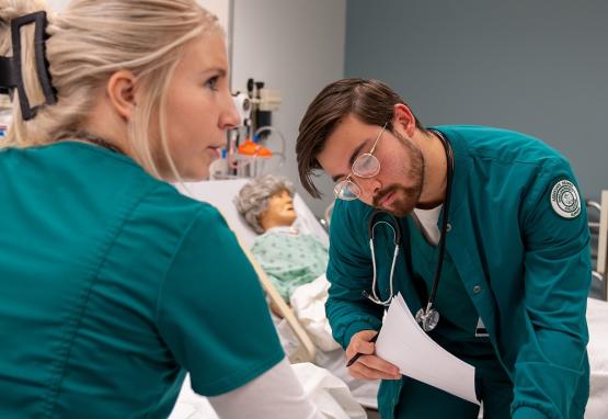  two nursing students work on a manikin 