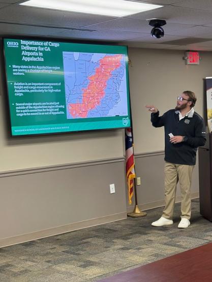 An individual gives a presentation while in front of a screen that says Importance of Cargo Delivery for GA Airports in Appalachia