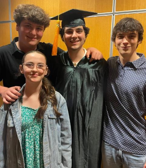 Peyton Wellman is shown wearing his graduation cap and robe while surrounded by family members and friends
