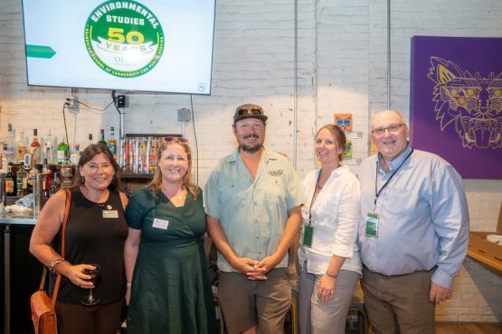 Tracy Plouck, Natalie Kruse-Daniels, Art Oestrike, Sara Davis and Geoff Dabelko stand together for a photo in front of the Environmental Studies 50th anniversary logo