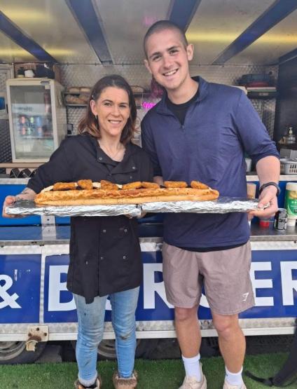 Jack Legath and another individual hold a plate with a long food item outside of a food truck