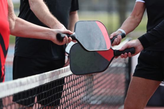 Pickleball players are shown holding their paddles together near the net