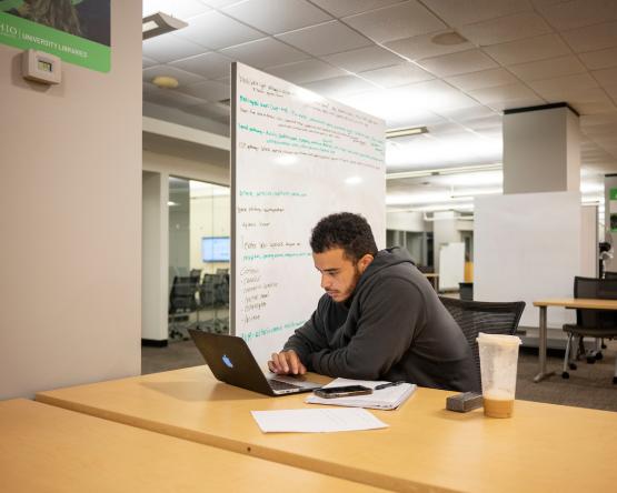 A student looks at a computer while sitting at a table in Alden Library