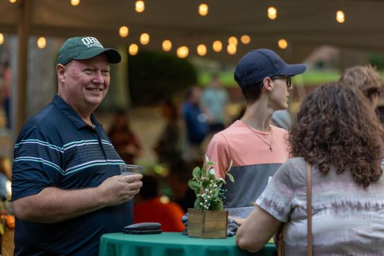 A Bobcat family member smiles while holding a drink during the Bobcat Family Welcome event on the College Green