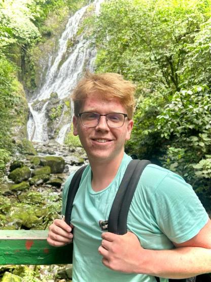 Student with glasses in front of waterfall with backpack