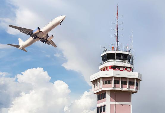 A plane flies next to an air traffic control tower.