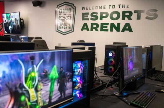 Computers in the foreground and a wall with "welcome to the esports arena" in the background. 