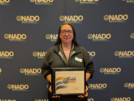An OHIO representative holds the Impact Award while standing in front of a media wall that says NADO