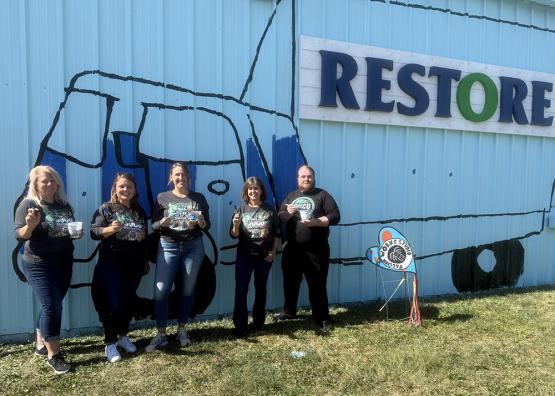 OUCU employees stand in front of a mural painted on the ReStore building