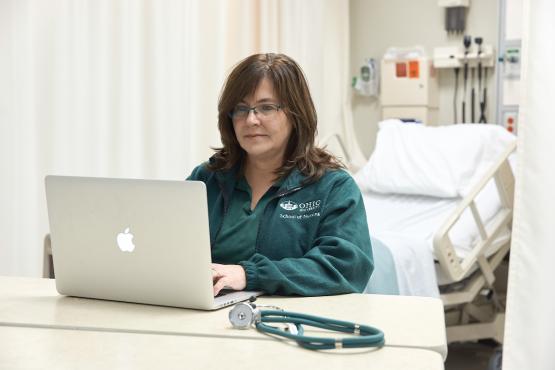 A nurse looks at a laptop in a hospital room