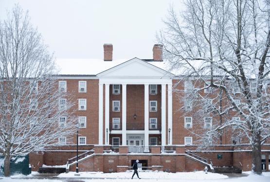 An OHIO building and the trees near it on the South Green are covered in snow. A student walks in front  of the building