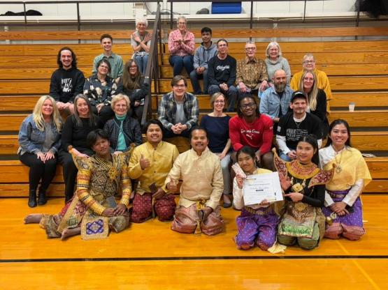 The members of the Moradokmai Theatre sit together on bleachers in a gymnasium at Ohio University