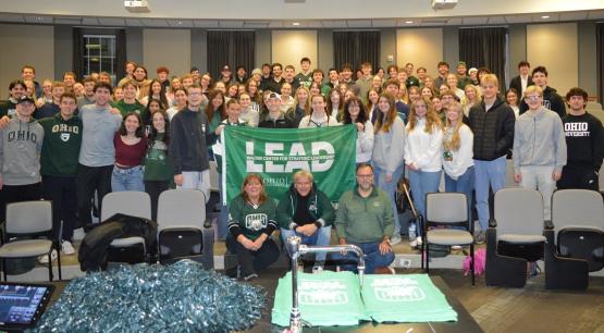 A large group of OHIO students and employees stand with Bas Baalmans and hold a green flag that says "LEAD"
