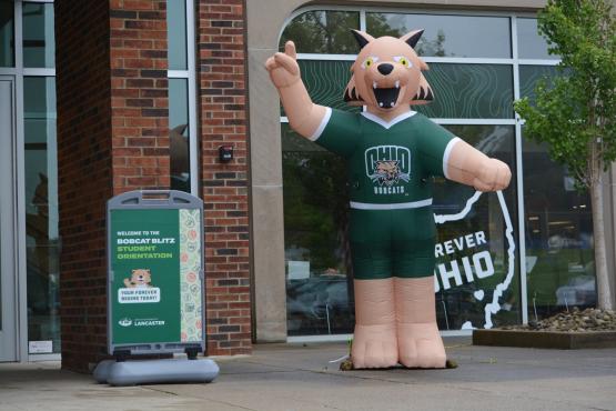 The outside of an OHIO Lancaster building with a sign for the Bobcat Blitz Student Orientation session and a figure of an OHIO mascot.