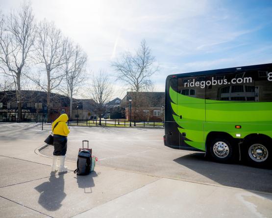 An OHIO student with a suitcase  waits outside of a GoBus parked near Baker University Center, Bird Arena and the Aquatic Center