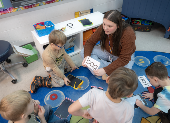 teacher candidate works with children to read notecards on carpet