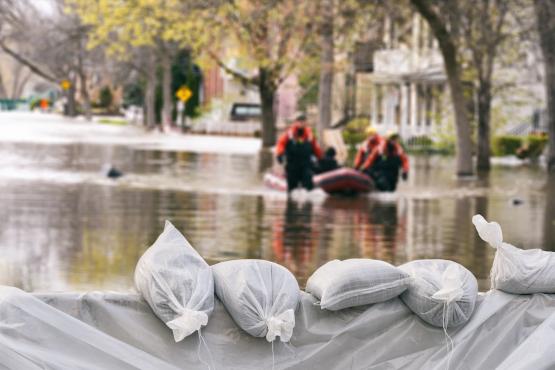 emergency workers wade through flood waters with sandbags in the foreground
