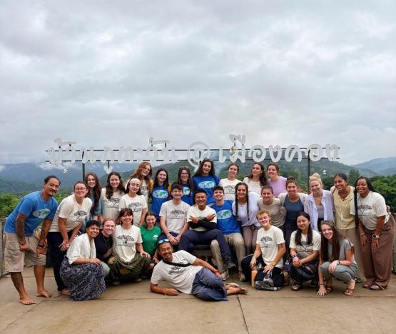 A group of people standing outside in front of a sign written in Thai.