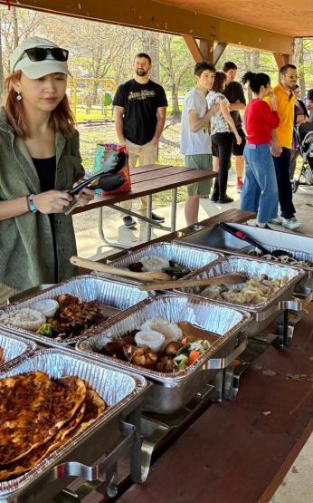 Trays of food are set on a table while people gather around at the Nowruz event