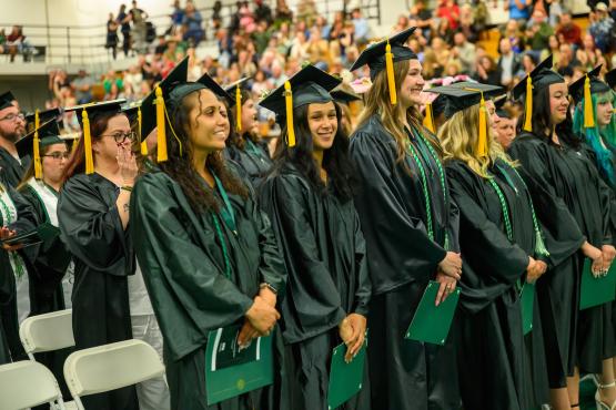 Graduating students stand in front of a large crowd at the Graduation Recognition Ceremony