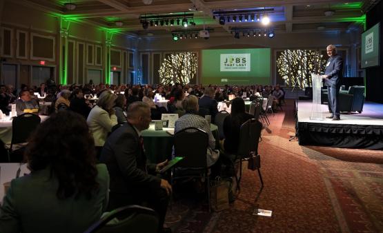 John Carey speaks in front of a large crowd in the Baker University Center at the State of the Region Conference