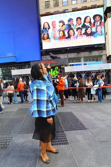 Dr. Lorraine Koobokile points at the billboard in Times Square that has her name and image on it