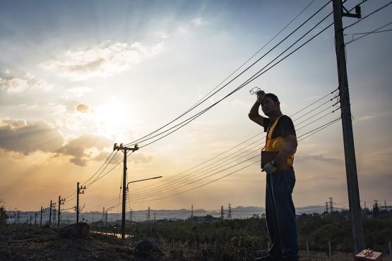 A power line worker wipes sweat off of his brow while standing in front of power lines.
