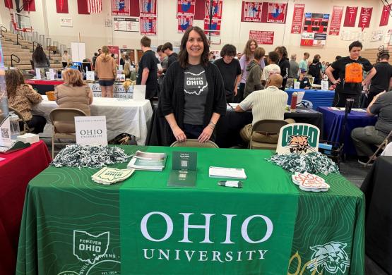 Jennifer Kellner-Muscar stands at an Ohio University booth at an event  inside a gymansium
