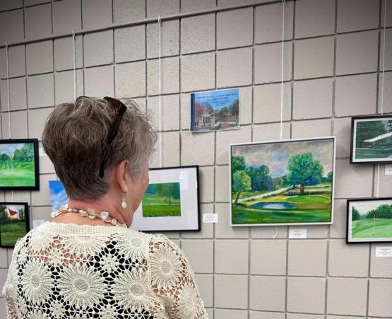 An individual looks over artworks hung on a wall at the Zanesville Art Show