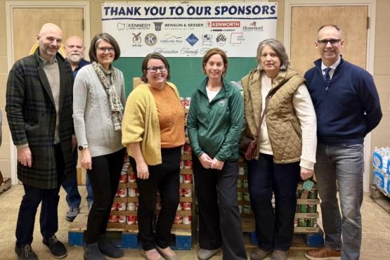 Representative of OHIO Chillicothe stand in front  of pallets filled  with cans of food,  while a sign behind them says "Thank you to our sponsors"