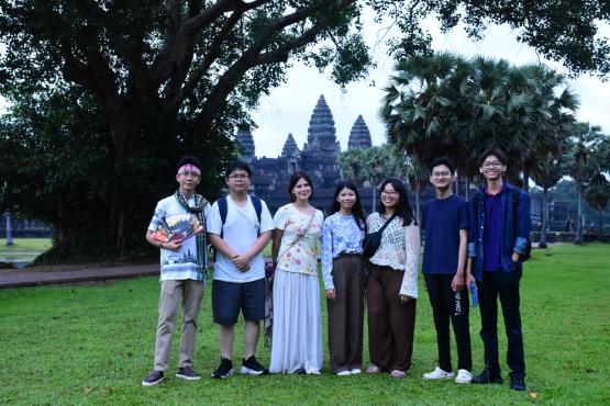 Andrea Tiu and Callia Fout stand with five other individuals outside in front of large trees and old buildings while in Cambodia