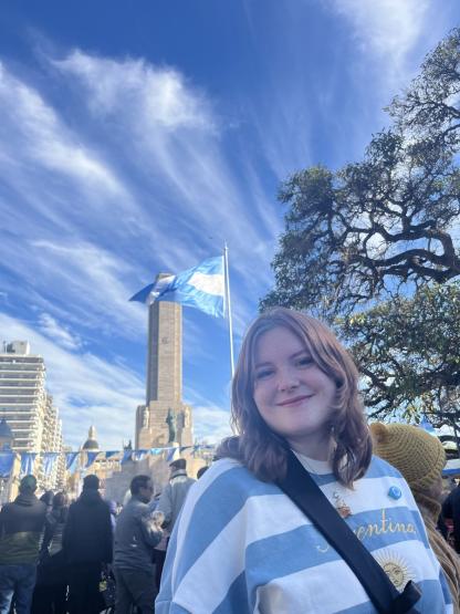 McKenna Thomas stands outside in Greece during her internship, and a flag flies behind her during a sunny day