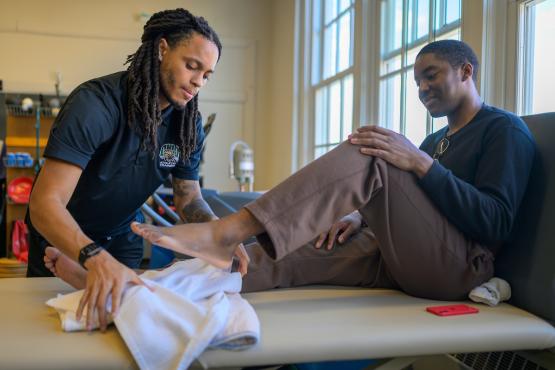 patient sitting on table with athletic trainer working on his leg