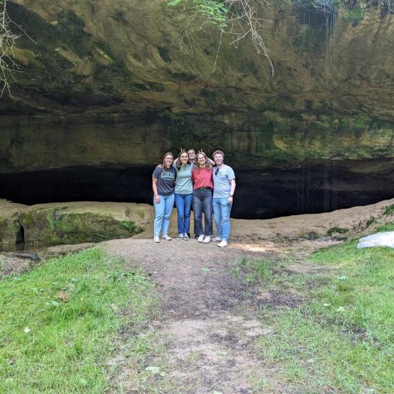 A group of students poses in front of a cave