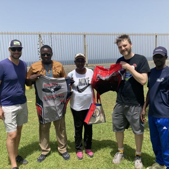 A group of people pose on a baseball field, holding up jerseys