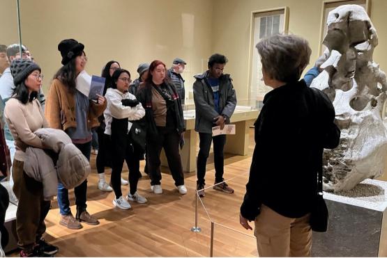 A group looks at a stone sculpture in a museum while a guide speaks to them