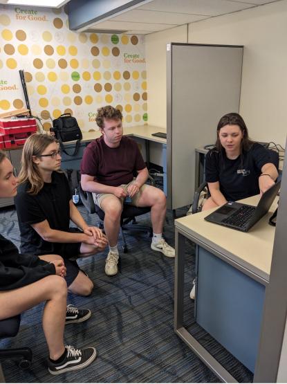 Three people look on as a fourth points to a laptop screen