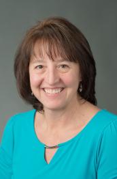 A smiling woman with brown hair poses in a studio 