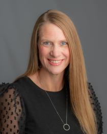 A woman wearing a black blouse smiles at the camera in a studio setting