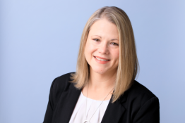 Donna Oklok smiles at the camera, wearing a white blouse and black blazer