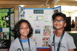 Two children pose for a picture in front of a STEM display