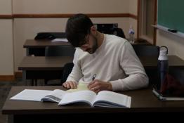 Male student writing on paper, seated at a desk