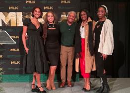 A group stands with their arms around each other in front of a background reading "MLK"