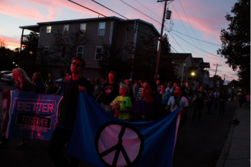 With their faces illuminated by police car lights, Ohio University students and Athens residents participate in the Interfaith Peace Walk through the city at sunset on Sept. 11, 2014