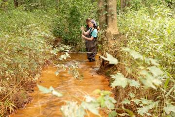 Ohio University engineering student Liz Myers (near) and Michelle Shively, Sunday Creek Watershed Coordinator at Rural Action, take water quality samples at Sunday Creek at an acid mine drainage discharge site in Truetown, Ohio.