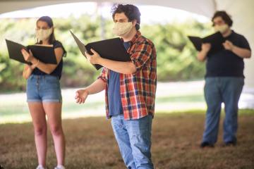 Students practice singing outside in a large tent for fear of indoor contact