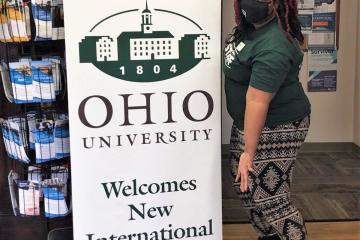 Shauna Torrington poses by sign that reads Ohio University Welcomes New International Students