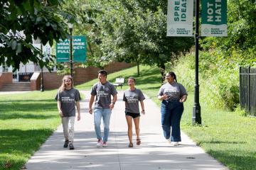 Four students walk along a sidewalk, with banners behind them that read "Spread Ideas, Not Hate" and "You can disagree respectfully"