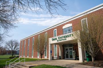 Outside exterior picture of a brick building that has a sign that reads "Ohio University Zanesville" on an arch doorway