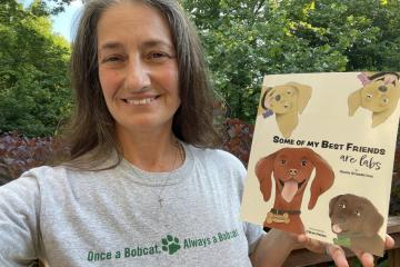 Gloria (Orlando) Ives, BSC ’88, shows off her Bobcat pride and her first book, which was designed by OHIO student-now-graduate CJ Herr, BFA ’22.
